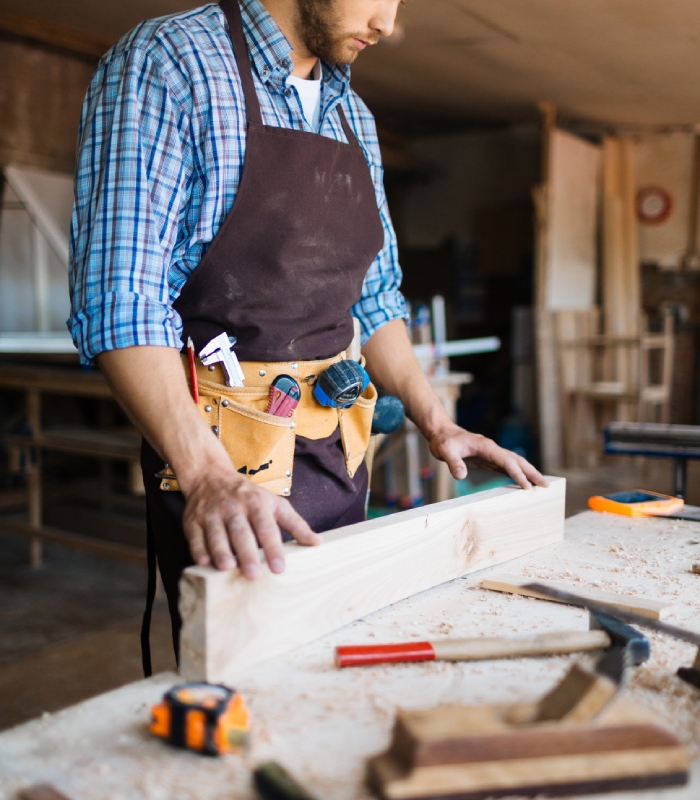 Charpentier préparant une pièce de bois sur un établi en atelier.