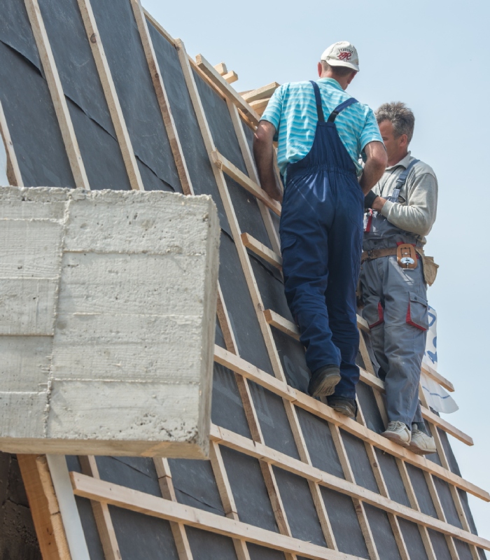 Deux couvreurs travaillant sur une toiture avec un écran sous-toiture et des liteaux en bois.