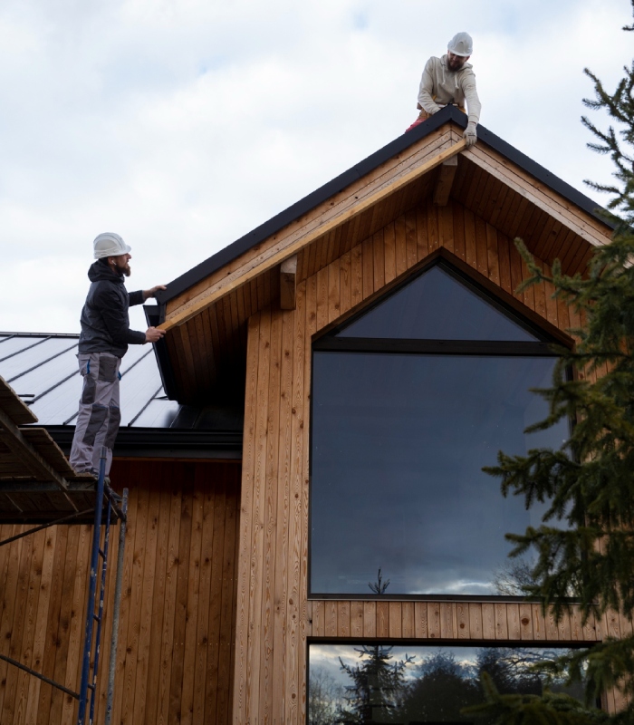 Deux couvreurs posant un habillage de rive sur une maison en bois